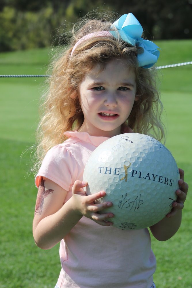 Avery Nilsson smiles big as she holds up a large souvenir golf ball she has signed by several players.